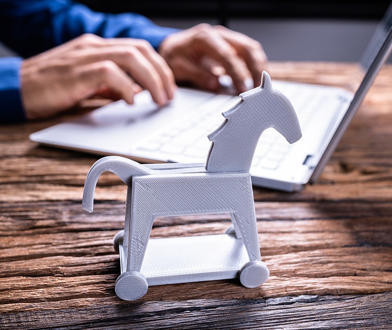Trojan horse model on a desk symbolizing Trojan viruses, with person typing on a laptop in the background, highlighting the theme of detecting and removing trojan viruses.