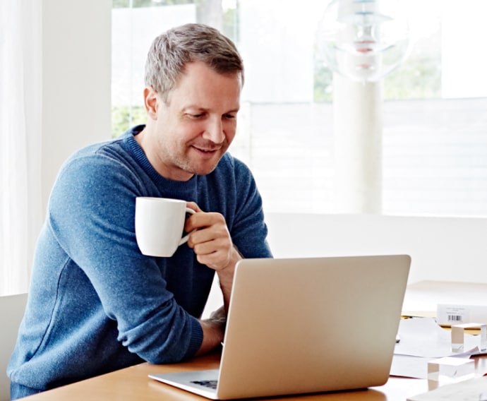 Man at home using laptop drinking coffee.